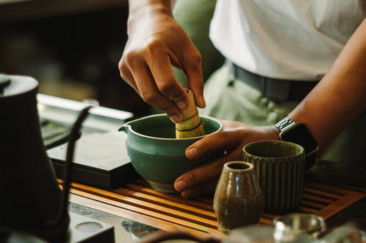 Preparing matcha tea by whisking powdered green tea in a bowl beside traditional teaware